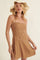 woman wearing a brown woven sundress with ruffle details and spaghetti straps, accessorized with a wide-brimmed hat