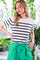 woman wearing a cream and navy striped short sleeve sweater with a green high-waisted skirt in a plant-filled setting