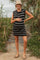 woman wearing a black and white striped maternity dress, holding her baby bump, standing outdoors among greenery
