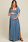 woman wearing a denim blue maternity maxi dress with short flutter sleeves and a smocked bodice, holding her baby bump