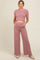 woman wearing a pink cropped maternity sweater and matching wide-leg pants, gently holding her baby bump