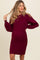 woman wearing a burgundy ribbed maternity dress with a fitted silhouette and puff sleeves, showing her baby bump
