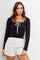 woman wearing a black ribbed long sleeve top with a scoop neck and white lace-up detail, paired with white sequin shorts