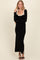 woman wearing a black long sleeve maxi dress with a nude scoop neckline and bow shoulder details, smiling at the camera