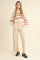 woman wearing a cream cable knit sweater with red accents and high-waisted beige wide-leg pants