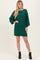 woman wearing a green cable knit sweater dress with balloon sleeves and black ankle boots