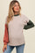 woman wearing a maternity knit sweater with beige body and green and rust long sleeves, showing her baby bump