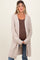 woman wearing a beige maternity cardigan over a brown ribbed tank top and holding her baby bump