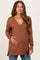 woman wearing a rust brown maternity sweater with a v-neck and side slits, showcasing her baby bump