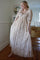 woman wearing a beige floral maxi dress with puff sleeves and a fitted bodice, posing in a bright room