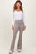 woman wearing a white long sleeve ribbed top and light gray flared pants, standing against a neutral background