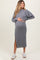 woman wearing a gray maternity sweater and matching midi skirt, gently holding her baby bump