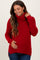woman wearing a red ribbed maternity sweater with a turtleneck and side slits, holding her baby bump