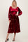 woman wearing a burgundy velvet midi dress with floral embroidery and long sleeves, standing in a relaxed pose