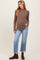 woman wearing a brown ribbed maternity sweater and light blue cropped jeans, holding her baby bump