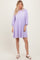 woman wearing a lilac puff sleeve dress with a smocked waist and a flared skirt, standing on a neutral background