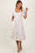 woman wearing a cream midi dress with puff sleeves and bow embroidery, smiling and posing with one hand raised