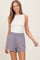 woman wearing a beige sleeveless top and gray relaxed-fit shorts with an elastic waistband