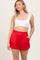 woman wearing a white cropped tank top and red elastic waist shorts with side pockets