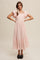 woman wearing a light pink midi dress with ruffle sleeves and a tiered hem, accessorized with a hair scarf