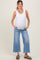 woman wearing a white ribbed maternity tank top and distressed light blue wide-leg jeans, showing her baby bump