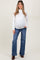 woman wearing a white long sleeve maternity top and blue flared jeans, showing her baby bump
