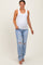 woman wearing a white ribbed maternity tank top and light blue distressed maternity jeans with a visible baby bump