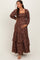 woman wearing a brown floral maternity maxi dress with long sleeves and ruffled tiers, gently holding her baby bump