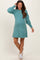 woman wearing a teal maternity sweater dress with puffed sleeves and a visible baby bump