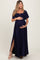 woman wearing a navy blue maternity maxi dress with a smocked bodice and a side slit, holding her baby bump