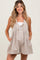 woman wearing a taupe maternity romper with pleated details and side pockets, smiling at the camera