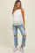 woman wearing a light beige sleeveless maternity top and distressed blue maternity jeans, showcasing her baby bump