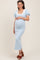 woman wearing a light blue maternity dress with puff sleeves and a square neckline, cradling her baby bump
