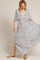 woman wearing a flowy white maxi dress with navy stripes and a deep v-neck, standing in a playful pose