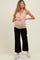 woman wearing a beige maternity tank top and black cropped pants, holding her baby bump