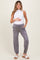 woman wearing a white sleeveless top and gray maternity jogger pants, holding her baby bump