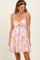 woman wearing a pink floral mini dress with a tie front and spaghetti straps