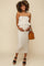 woman wearing a beige strapless maternity dress with a ruffled hem and holding her baby bump