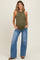woman wearing a dark olive green maternity tank top and light blue wide-leg jeans, holding her baby bump