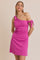 woman wearing a hot pink one-shoulder mini dress with tie details on the sleeves
