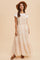 woman wearing a peach tiered maxi dress with lace detailing and a white top, accessorized with a wide-brimmed hat