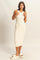 woman wearing a cream ribbed knit midi dress with a scoop neckline and side slits, paired with white slide sandals
