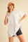 woman wearing an oversized white t-shirt and black shorts, posing with one hand on her hip and wearing a cap