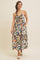 woman wearing a floral midi dress with a sweetheart neckline and adjustable straps, standing with hands in pockets