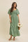 woman wearing a green square neck maxi dress with flutter sleeves and a tiered skirt, holding a woven basket with flowers
