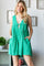 woman wearing a green sleeveless dress with a deep V-neckline and front pockets, standing against a light background