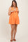 woman wearing an orange maternity romper with a tie detail and empire waist, showing off her baby bump