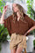 woman wearing a brown oversized button-up shirt and beige high-waisted shorts, accessorized with a wide-brimmed hat