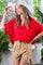 woman wearing a red oversized button-up shirt and tan high-waisted shorts, styled with a large white hat