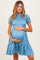 woman wearing a blue maternity dress with short sleeves, smocked bodice, and ruffled hem, holding her baby bump